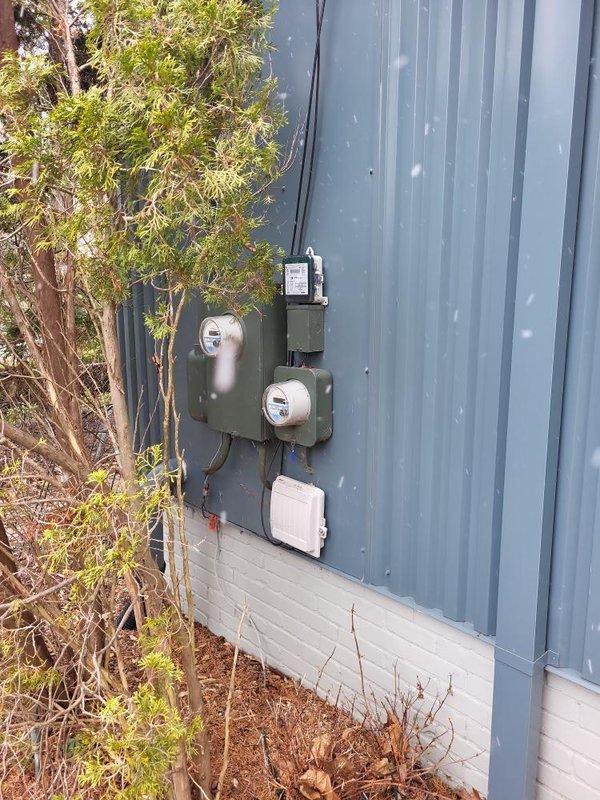 # Electrical Estimate - Generator Installation

Conducted comprehensive site assessment for new whole home generator installation at residential property with corrugated metal siding and existing electrical service infrastructure. Evaluated current electrical service configuration including meter base, service entrance conductors, and overhead utility connection points to determine optimal generator placement and integration requirements.

Documented existing electrical infrastructure consisting of dual meter housings, exterior-mounted disconnect equipment, and conduit routing along building exterior. Assessed available space on side wall adjacent to service entrance for generator pad placement and transfer switch installation. Identified clear access pathway for fuel line connection and verified adequate clearance from building openings per manufacturer specifications and local code requirements.

Analyzed electrical service capacity and load requirements to properly size automatic tr