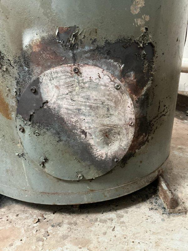 Performed CSD1 inspection and comprehensive cleaning on single commercial boiler unit located inside shop. Upon arrival, found significant soot and combustion byproduct accumulation within combustion chamber and flue passages, indicating extended operation without maintenance. Access panel and exterior surfaces exhibited heavy rust staining, corrosion, and paint deterioration consistent with moisture exposure and aging equipment.

Conducted thorough internal cleaning of combustion chamber, removing heavy carbon deposits and debris from chamber walls and surfaces. Cleaned and inspected burner assembly, flue passages, and heat exchanger sections. Evaluated hex nut and bolt assemblies showing signs of corrosion and tarnishing. Assessed structural integrity of tank base and circular access panel, noting advanced rust penetration and pitting in multiple areas. Documented extensive corrosion patterns on access cover plate and surrounding metal surfaces with rust bleeding through painted exte