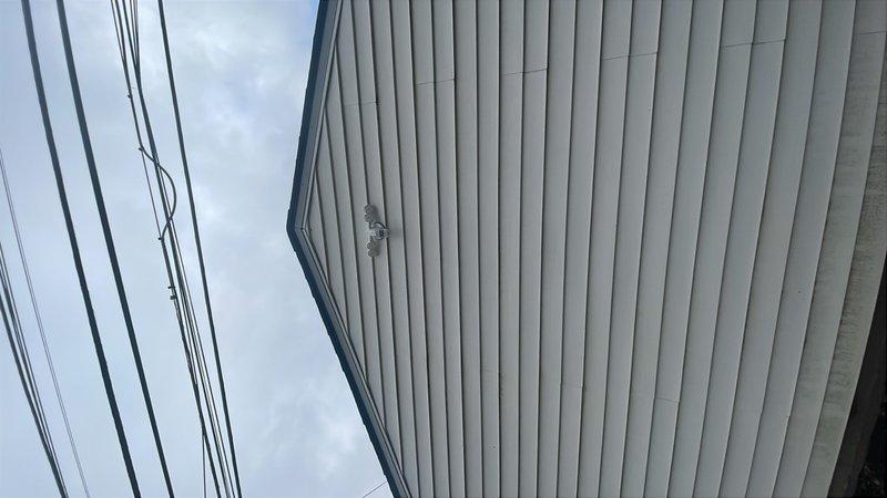 Completed site assessment and documentation for sold repair work on building exterior electrical system. Inspected overhead utility service connections and building-mounted exterior lighting fixture on vertical metal siding. Accessed attic space to evaluate interior electrical routing and structural framing conditions in preparation for upcoming repair work. Photographed existing conditions including service entrance cables, wall-mounted fixtures, and attic framing to document pre-repair status. Repair work scheduled pending arrival of required materials and components.