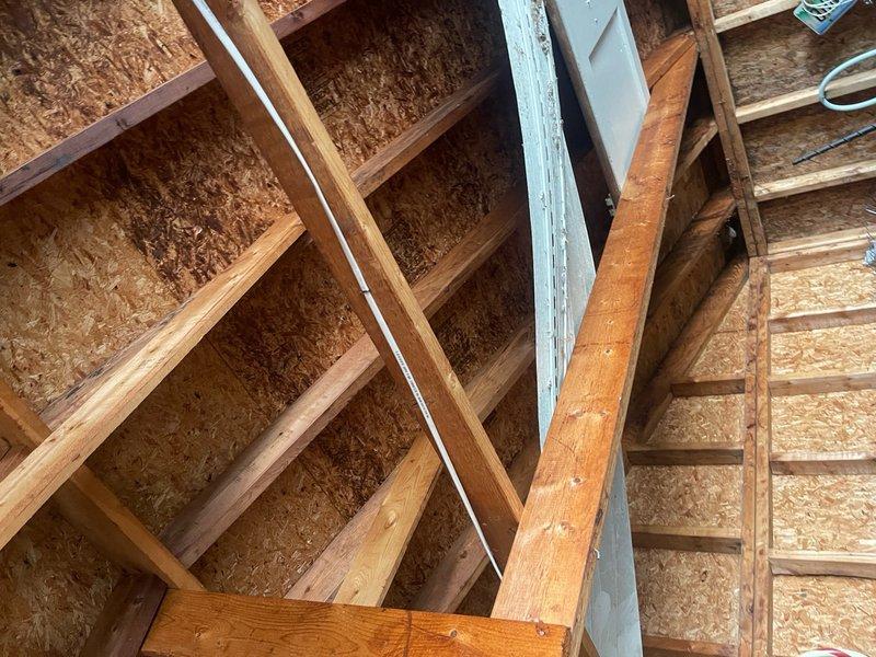 Completed site assessment and documentation for sold repair work on building exterior electrical system. Inspected overhead utility service connections and building-mounted exterior lighting fixture on vertical metal siding. Accessed attic space to evaluate interior electrical routing and structural framing conditions in preparation for upcoming repair work. Photographed existing conditions including service entrance cables, wall-mounted fixtures, and attic framing to document pre-repair status. Repair work scheduled pending arrival of required materials and components.