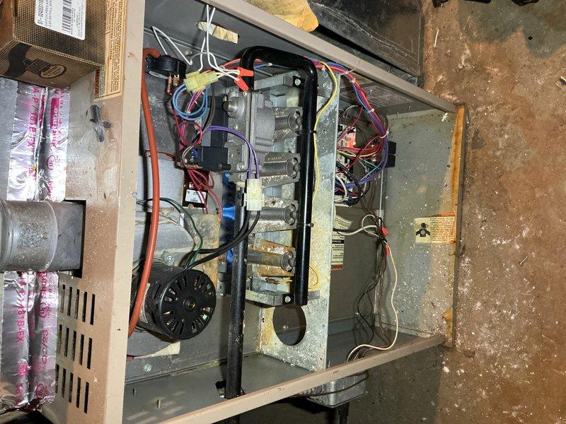 Responded to service call for 10+ year old furnace in basement blowing cold air. Performed diagnostic inspection of gas furnace and air handler unit, examining internal components including heating elements, control board, electrical connections, and gas valve assembly. Identified issue with heating system operation, inspected all wiring connections (multiple circuit wires including red, orange, purple, yellow, black, and white leads), verified gas supply connections, and assessed overall equipment condition showing age-related wear and dust accumulation.