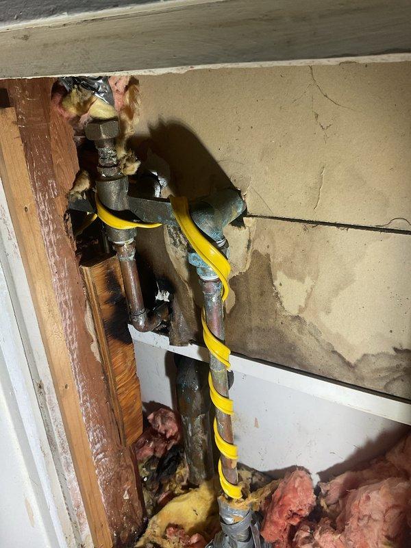 Responded to service call for leaking shower valve in residential bathroom. Upon arrival, inspected four-handle shower/tub valve assembly mounted on white tiled wall. Accessed plumbing system through wall cavity to diagnose source of leak. Inspection revealed aging valve components and corroded pipe fittings within wall structure. Exposed plumbing infrastructure showed signs of wear consistent with leak symptoms reported by homeowner. Documented existing conditions via photography for service records. Assessed valve assembly and determined repair requirements for proper resolution of leaking condition.