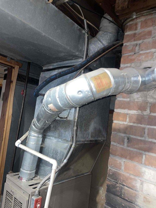 Completed furnace replacement estimate for duplex property with two natural gas furnaces located in basement. Both 10+ year old units found to have cracked heat exchangers, with one unit also experiencing blower motor failure, rendering systems unsafe for operation. Documented existing equipment configuration including ductwork connections, PVC condensate lines, and venting systems installed against brick foundation wall.