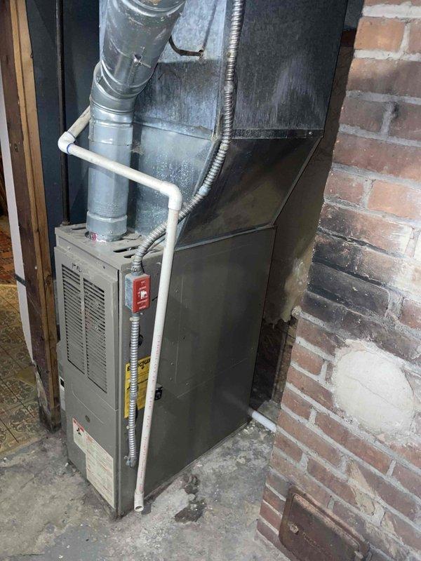 Completed furnace replacement estimate for duplex property with two natural gas furnaces located in basement. Both 10+ year old units found to have cracked heat exchangers, with one unit also experiencing blower motor failure, rendering systems unsafe for operation. Documented existing equipment configuration including ductwork connections, PVC condensate lines, and venting systems installed against brick foundation wall.