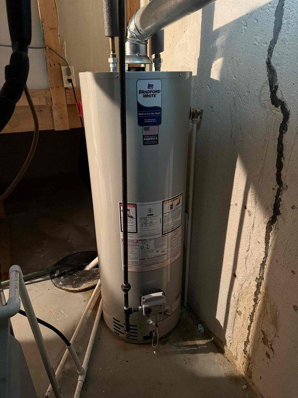 Completed installation of a 40-gallon standard Bradford White water heater in basement utility area. Installed new unit with proper venting through black exhaust pipe routed to ceiling, connected all water supply lines and gas connections, and verified proper operation of gas control valve and all safety features.