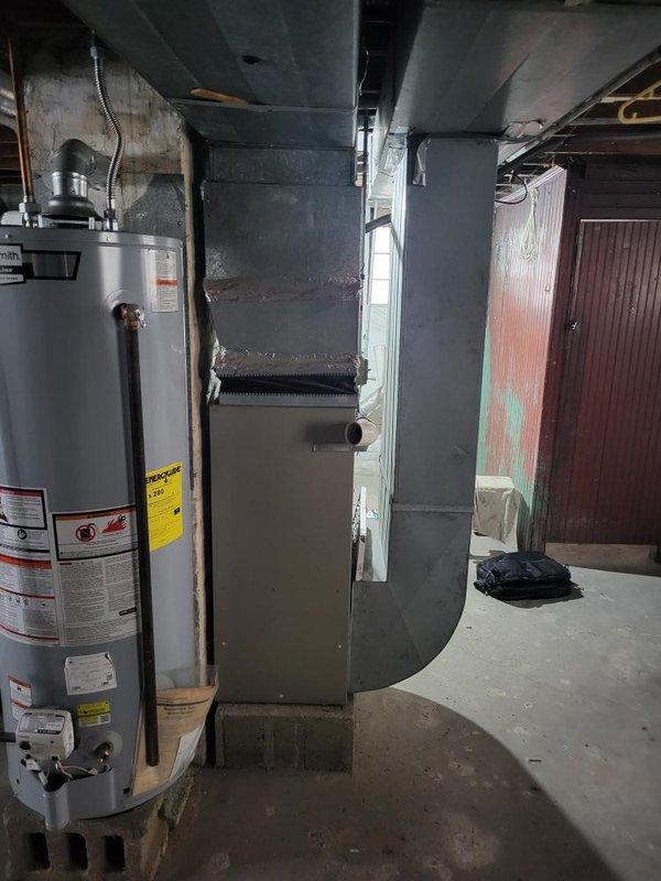 Completed on-site assessment of existing HVAC system and water heating equipment in basement mechanical room for replacement estimate. Documented current furnace unit with overhead ductwork configuration and two water heaters (one white/cream colored, one gray) installed against concrete block walls. Photographed equipment conditions, piping connections, electrical infrastructure, and spatial layout to provide accurate replacement specifications and equipment sizing recommendations.