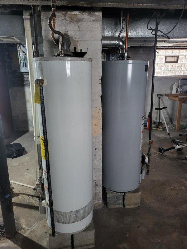 Completed on-site assessment of existing HVAC system and water heating equipment in basement mechanical room for replacement estimate. Documented current furnace unit with overhead ductwork configuration and two water heaters (one white/cream colored, one gray) installed against concrete block walls. Photographed equipment conditions, piping connections, electrical infrastructure, and spatial layout to provide accurate replacement specifications and equipment sizing recommendations.