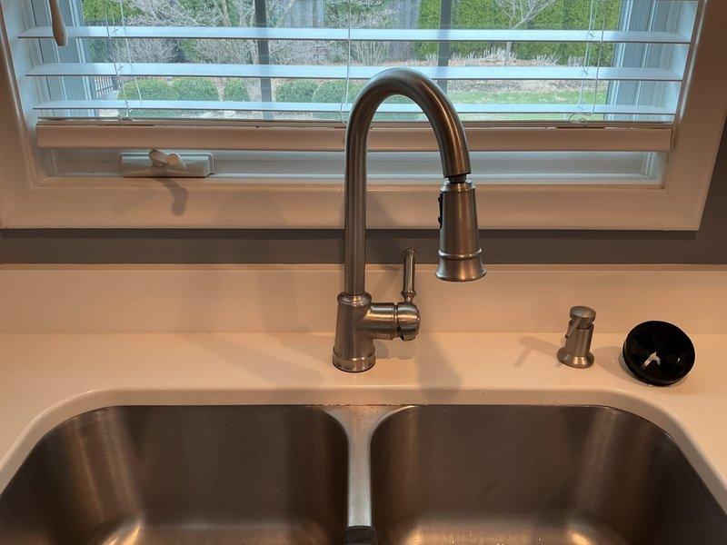 Completed installation of customer-supplied kitchen faucet and garbage disposal unit. Installed brushed nickel pull-down faucet with single lever handle above double-basin stainless steel undermount sink. Connected hot and cold water supply lines, ensuring proper water pressure and testing for leaks. Mounted matching soap dispenser on countertop deck. Installed garbage disposal unit beneath sink basin with proper electrical connection to air switch mounted on counter surface. Verified all components functioning properly with no leaks detected. System tested and operational upon completion.
