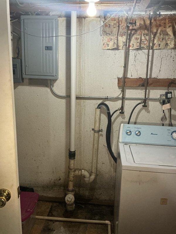 Responded to reported plumbing issues including kitchen sink drainage leaking into basement and reduced hot water flow in basement shower. Performed diagnostic inspection of basement plumbing system, examining vertical drainage lines, supply piping, and connections near laundry area. Identified compromised drain line penetration through floor joists with evidence of active water infiltration and moisture damage to surrounding structural components. Inspected shower mixing valve and supply lines, noting restriction in hot water line affecting flow rate while cold water supply maintained normal pressure. Evaluated PVC drainage system routing from upper level fixtures, observing improper sealing at floor penetration points allowing water migration during kitchen sink and dishwasher discharge cycles. Documented condition of plumbing infrastructure including corroded metal components at ceiling joists and moisture staining on concrete floor near drain assembly. Provided assessment findings 