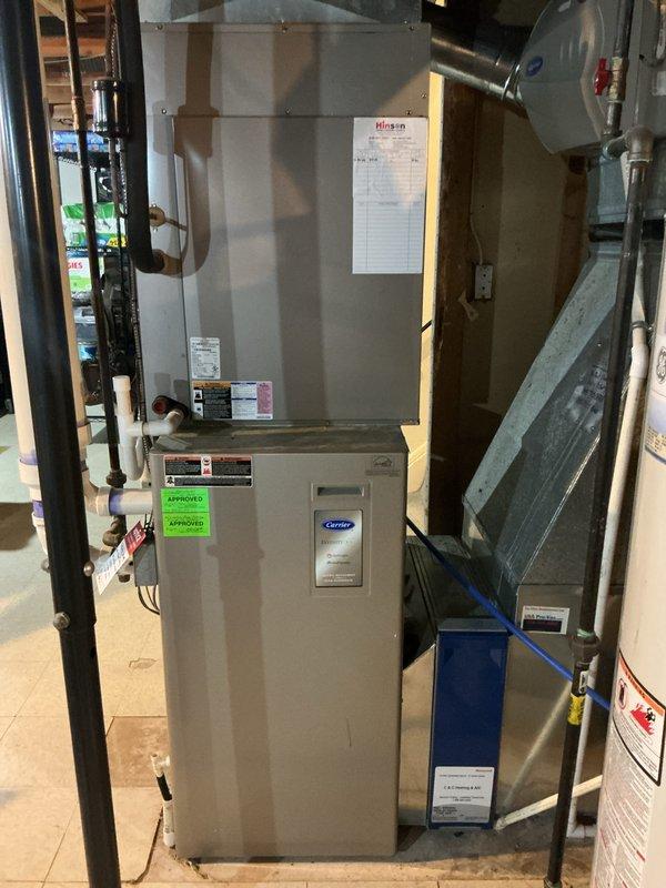 Conducted comprehensive assessment of existing 12-year-old Carrier furnace and air conditioning system in basement mechanical room to provide replacement estimate. Documented current equipment configuration, including air handler unit, ductwork connections, and associated mechanical components. Photographed existing HVAC installation showing furnace positioning, duct routing, copper piping connections, and available clearances for future equipment replacement planning.