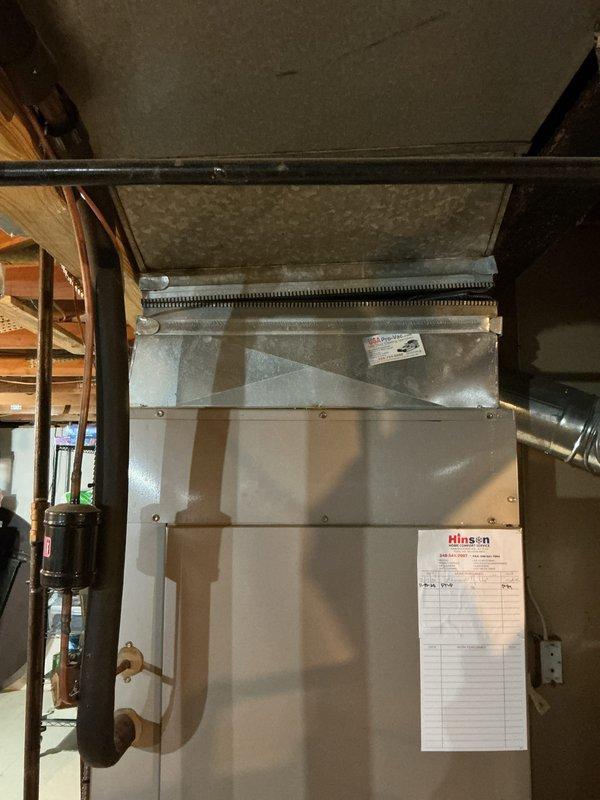 Conducted comprehensive assessment of existing 12-year-old Carrier furnace and air conditioning system in basement mechanical room to provide replacement estimate. Documented current equipment configuration, including air handler unit, ductwork connections, and associated mechanical components. Photographed existing HVAC installation showing furnace positioning, duct routing, copper piping connections, and available clearances for future equipment replacement planning.