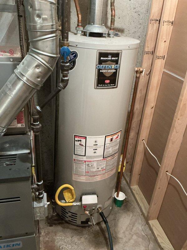 Installed a 40-gallon Bradford White Defender Safety System tanked water heater in residential basement utility area. Reconnected all copper supply and discharge piping, installed appropriate shut-off valves with blue-handled controls, and secured metallic flue vent ductwork to ensure proper exhaust ventilation. Completed gas line connection using flexible yellow connector, verified all connections for proper operation and code compliance.