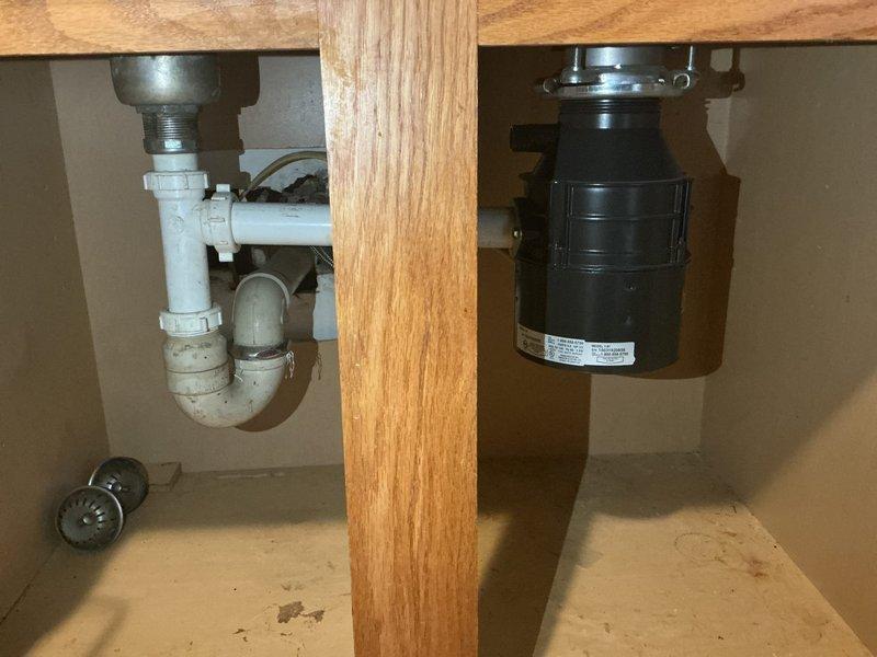 Responded to non-functional garbage disposal in first-floor kitchen sink of 1950s-era home. Upon inspection, found existing black garbage disposal unit mounted under sink with standard drain configuration and P-trap assembly. Assessed unit for electrical connectivity, mechanical jamming, and reset functionality. Disposal showed signs of age and wear consistent with original installation timeline. Restored unit to working condition through troubleshooting and repair procedures. Verified proper drainage, mounting security, and operational performance before completion.