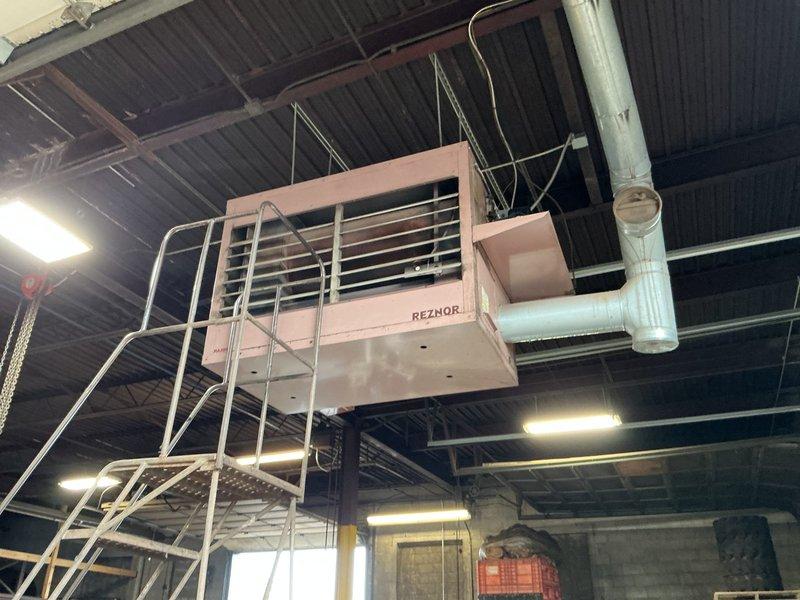Performed service call on Reznor RA350 oil-fired furnace unit located in commercial facility requiring ladder access. Inspected ceiling-mounted unit with horizontal louver discharge grille and verified proper safety railing installation around equipment. Documented unit condition and configuration, noting this is one of five total units on-site requiring future preventive maintenance scheduling. Unit accessible from ground level with ladder, positioned near corrugated metal ceiling structure with white ductwork distribution system.