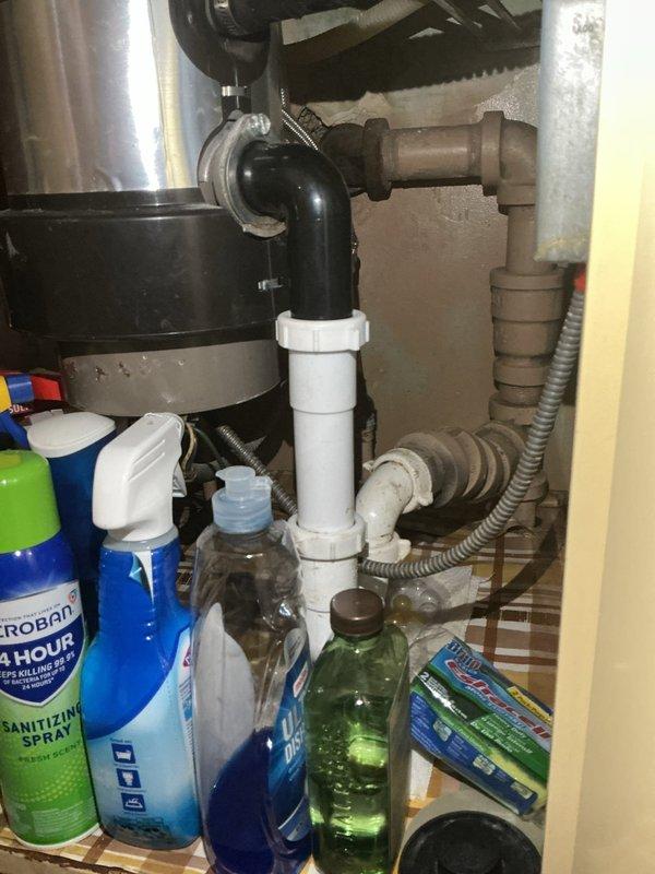 Responded to kitchen sink backup complaint and performed diagnostic inspection of drainage system. Upon arrival, inspected under-sink plumbing configuration and identified issues with drain assembly and trap connections. Examined the existing black trap pipe, white PVC drain lines, and associated fittings for proper installation, blockages, and potential points of failure. Assessed water supply lines and flexible connections for any contributing factors to the drainage problem. Cleared blockage from kitchen sink drain and verified proper water flow through the system, restoring full drainage functionality.