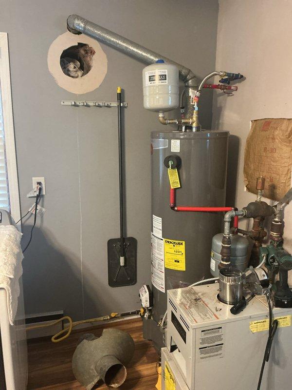 Responded to emergency service call for furnace with compromised exhaust venting system. Upon inspection, discovered significant rust deterioration on metal venting pipe connected to furnace, resulting in a breach that posed carbon monoxide hazard. Furnace was immediately shut down to prevent dangerous exhaust fumes from entering living space. Documented existing conditions with photographs showing the deteriorated ductwork elbow fitting at ceiling penetration point and overall mechanical room configuration including water heater, furnace unit, and associated plumbing components. Advised customer of safety concerns and recommended immediate venting system replacement before furnace could be safely returned to operation.