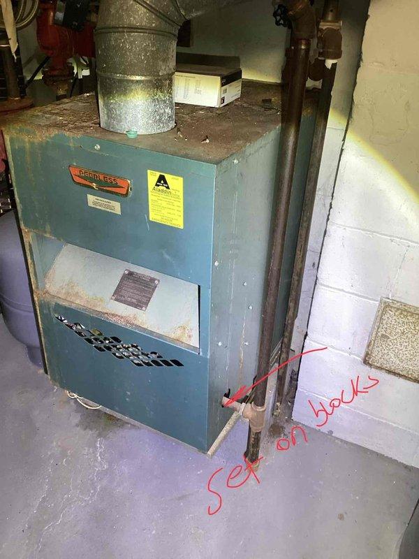 Conducted comprehensive assessment of residential boiler system exceeding 75 years of service life in basement mechanical room. Documented existing Peerless brand unit showing significant age-related deterioration, including extensive surface corrosion, rust streaking on cabinet panels, and compromised structural integrity of metal casing. Noted disconnected expansion tank with visible markings indicating non-operational status, along with aged copper piping exhibiting oxidation and outdated electrical connections requiring replacement. Provided detailed photographic documentation and recommended complete boiler system replacement due to equipment age, safety concerns, and inefficiency of existing installation.