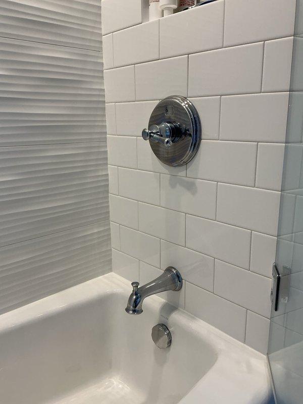 Completed installation of bathroom shower and tub fixtures including chrome shower control valve with cross-handle design, tub spout, and drain overflow cover plate on newly tiled subway tile wall. Additionally installed three-piece vanity sink assembly in bathroom and tightened loose kitchen faucet to restore proper function. All fixtures tested for proper operation and verified no leaks present upon completion.