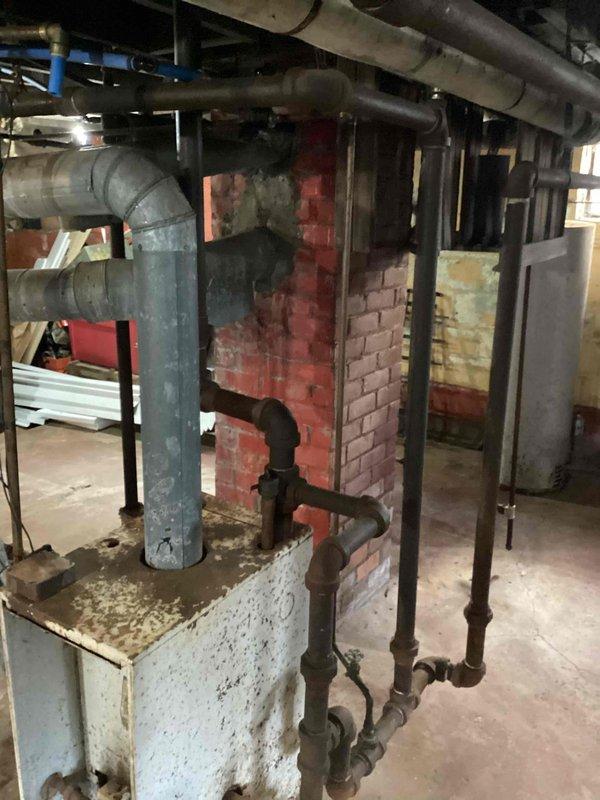 Provided estimate for complete steam boiler replacement due to flood damage and age-related deterioration of existing 10+ year old unit. Existing boiler system showed extensive corrosion, rust staining, and water damage throughout, rendering equipment beyond economical repair. Deteriorated chimney structure exhibited significant brick damage and structural compromise requiring attention during replacement process.