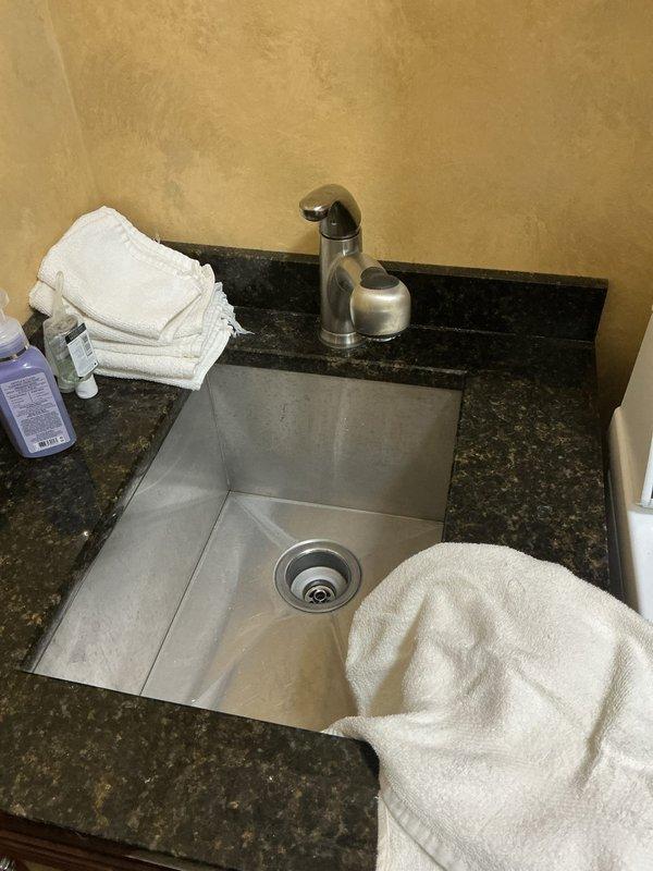 Responded to water leak complaint originating from laundry sink area. Upon arrival, conducted thorough inspection of sink plumbing system and cabinet interior. Examined P-trap assembly, drain connections, and supply line configuration for signs of active leakage or moisture damage. Verified integrity of chrome drain assembly, white PVC P-trap, and all connection points. Inspected black flexible supply hoses and shut-off valves for potential leak sources. Placed collection container beneath plumbing assembly as precautionary measure. Assessed undermount sink installation and faucet connections for any contributing factors. All plumbing components were evaluated and leak source was identified and addressed to restore proper function.