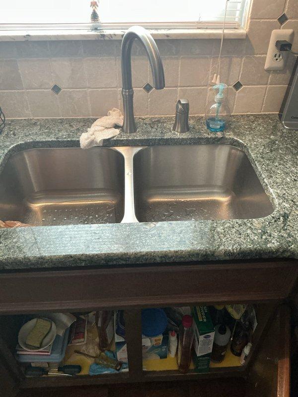 Responded to service call for multiple plumbing issues including kitchen sink leak, basement faucet replacement needs, and reduced shower pressure. Performed diagnostic inspection of kitchen sink plumbing system, identifying leak source at drain assembly and P-trap connections beneath double-basin stainless steel sink. Inspected under-sink plumbing configuration including PVC drain lines, compression fittings, and shut-off valves to assess leak points and determine necessary repairs for proper drainage function.