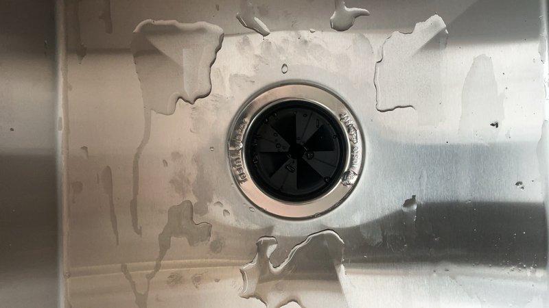 Responded to service call for plumbing system evaluation and documentation. Inspected bathroom sink basin showing extensive porcelain deterioration and coating failure around drain assembly with chrome trim and plastic propeller-style drain cover. Documented utility pump system installation featuring black motor unit with metallic mounting flanges connected to white PVC piping configuration on wooden mounting board within utility cabinet. Photographed complete plumbing assembly including connection points, fittings, and electrical components for service records per special instructions.