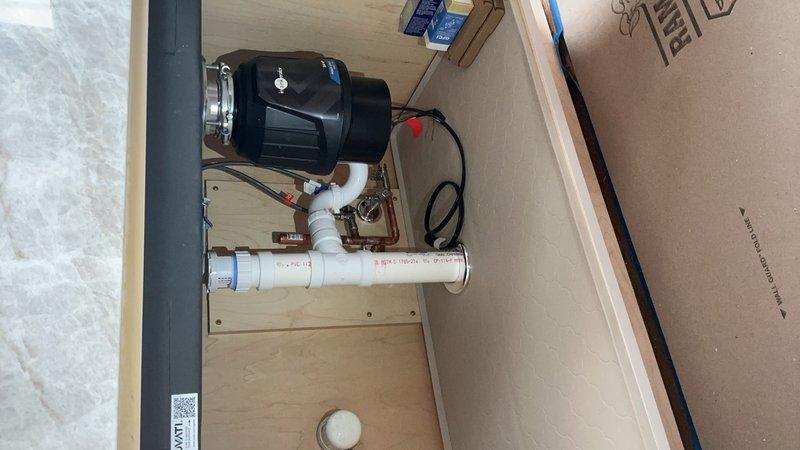 Responded to service call for plumbing system evaluation and documentation. Inspected bathroom sink basin showing extensive porcelain deterioration and coating failure around drain assembly with chrome trim and plastic propeller-style drain cover. Documented utility pump system installation featuring black motor unit with metallic mounting flanges connected to white PVC piping configuration on wooden mounting board within utility cabinet. Photographed complete plumbing assembly including connection points, fittings, and electrical components for service records per special instructions.