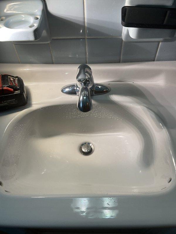 Responded to a plumbing service call for bathroom sink maintenance. Upon inspection, serviced a traditional two-handle chrome faucet and white porcelain sink assembly. Verified proper operation of the drain stopper mechanism and inspected the P-trap assembly beneath the sink, confirming all PVC drain connections and chrome tailpiece were secure and leak-free. Checked both hot and cold water supply lines with mounting brackets for proper connection to the faucet assembly. All plumbing components were found to be in standard working condition with no visible leaks or damage detected.