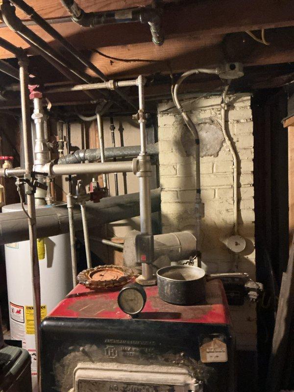 Conducted estimate for boiler replacement in basement utility room. Inspected existing aged heating unit with red-painted body and black metal front panels showing significant wear and corrosion. Documented current system configuration including associated piping, water heater, and distribution components. Photographed equipment and provided replacement recommendations to homeowner.