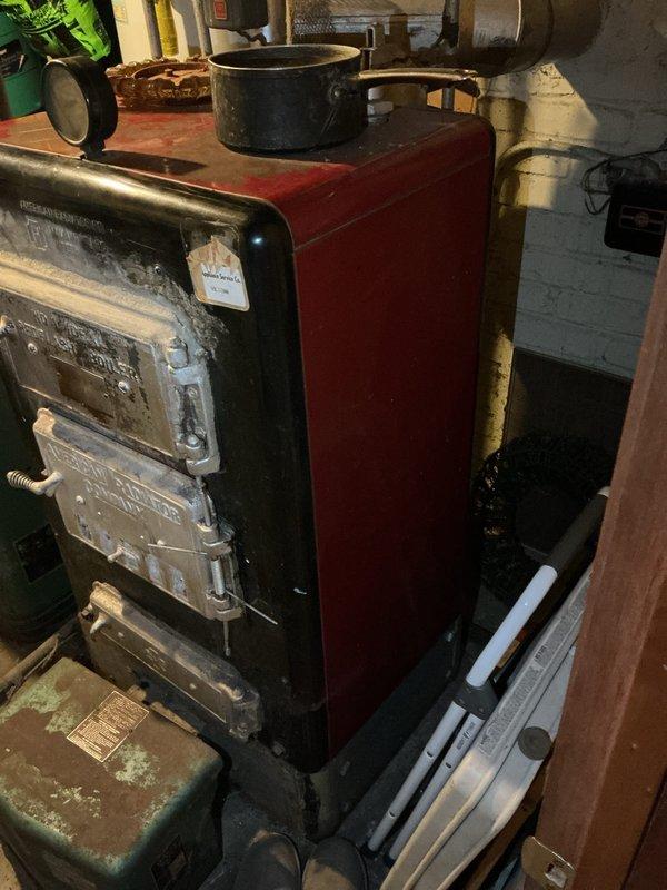 Conducted estimate for boiler replacement in basement utility room. Inspected existing aged heating unit with red-painted body and black metal front panels showing significant wear and corrosion. Documented current system configuration including associated piping, water heater, and distribution components. Photographed equipment and provided replacement recommendations to homeowner.