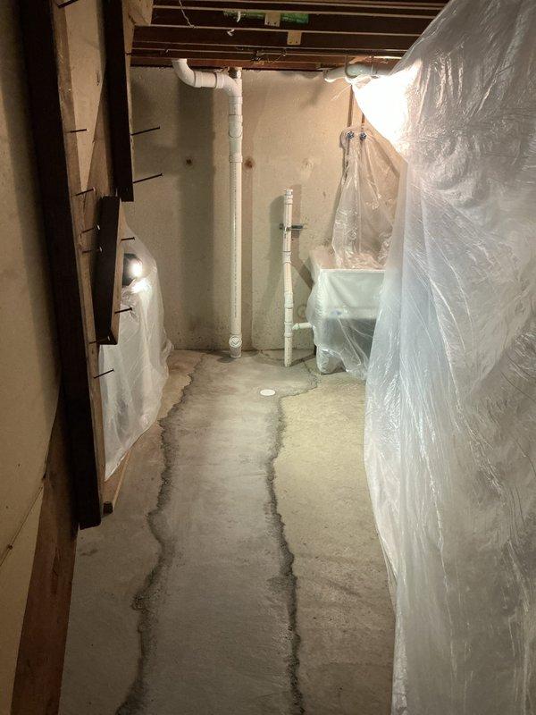 Responded to callback for basement plumbing installation inspection. Documented newly installed white PVC drainage and vent piping system running vertically through unfinished basement space during active renovation phase. Verified proper pipe placement and securing methods through plastic vapor barrier and wall framing, confirmed system integration with existing infrastructure, and photographed concrete floor conditions showing recent pouring work with visible seam lines for customer records.