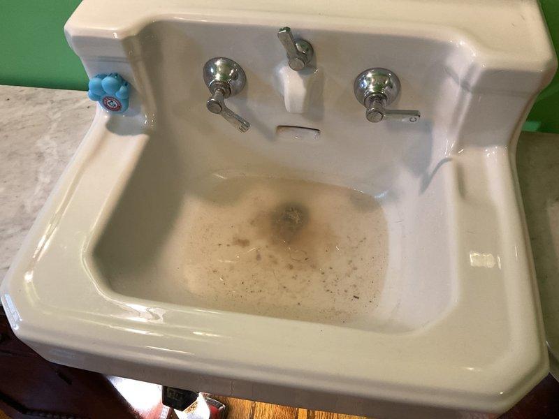 Responded to a chronic drainage issue in a third-floor bathroom that had persisted for approximately six months. Upon inspection, found a vintage wall-mounted ceramic sink with significant staining and buildup in the basin, indicating long-term slow drainage problems. Examined the drain assembly and P-trap configuration beneath the sink, which consisted of chrome tailpiece connected to white plastic P-trap with rubber coupling and metal clamps. Assessed the condition of all plumbing connections, drain lines, and trap assembly for blockages, improper venting, or deterioration. The aging fixture showed considerable wear and staining consistent with extended use and potential mineral deposit accumulation. Documented existing conditions of the vintage sink, drain assembly, supply connections, and overall plumbing configuration. Due to the age and condition of the fixture, recommended consideration for sink replacement as a long-term solution to prevent recurring drainage issues and improve