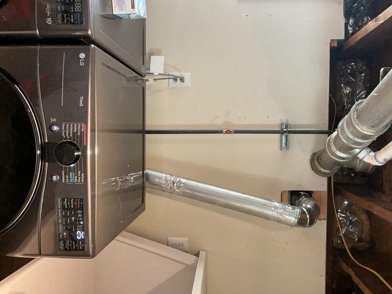 Responded to a laundry room service call to address dryer venting concerns. Upon inspection, identified improper dryer vent configuration with flexible aluminum ducting and inadequate routing from the appliance to the exterior termination point. Accessed the ceiling cavity above the laundry area to assess the existing vent pathway and structural limitations. Documented the current installation showing the LG front-loading washing machine placement, existing wall-mounted vent components, and the flexible white ribbed ducting material. Photographed the overhead framing, joists, and existing utility lines to plan proper vent routing that complies with code requirements for rigid or semi-rigid metallic ductwork with minimal bends and appropriate clearances from electrical wiring and insulation. Provided recommendations for correcting the ventilation system to ensure proper airflow, reduce lint accumulation risk, and improve dryer efficiency and safety.