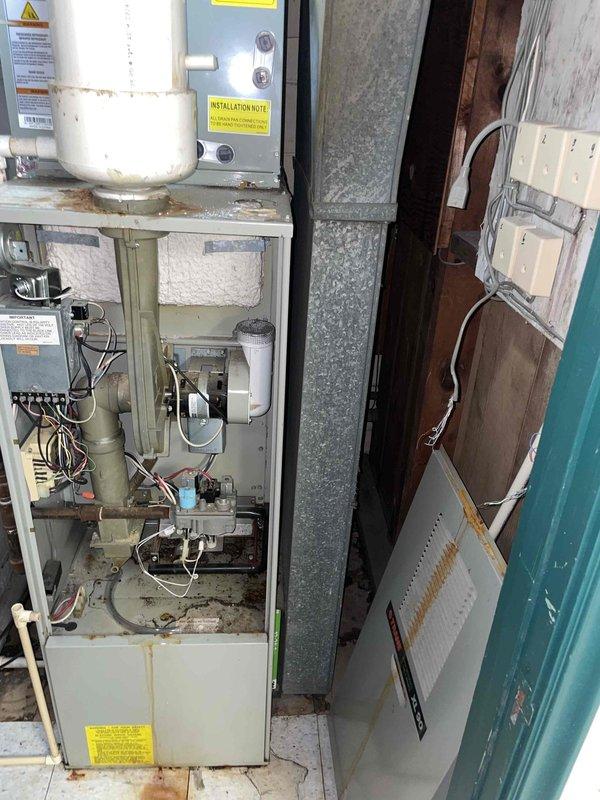 Conducted comprehensive assessment of basement HVAC system for replacement estimate including aging furnace and hot water tank. Existing natural gas furnace showing active refrigerant leaks, limited heating capacity to single room only, and significant deterioration with rust staining and accumulated debris in cabinet and base pan. Hot water tank identified as original equipment from 1990s requiring replacement. Documented condition of 15-year-old furnace installation in utility closet with open access panels revealing internal components, blower assembly, wiring, and control systems showing signs of age and wear. Photographed equipment configuration including ductwork, electrical connections, and mechanical room layout to provide accurate replacement specifications for dual-furnace residential system.