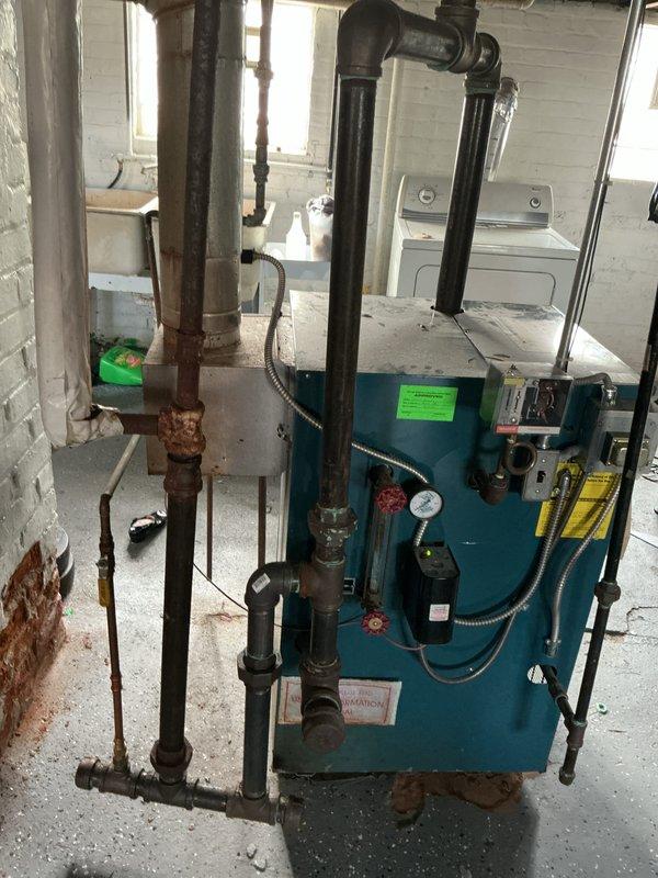 Responded to service call for steam boiler system experiencing pilot light failure and flashing programmable feeder indicator. Performed diagnostic inspection of basement-located steam boiler unit and discovered cracked heat exchanger. Observed extensive corrosion and deterioration on supply piping throughout system. Documented equipment condition with photographic evidence showing compromised heat exchanger, corroded vertical piping, and overall system age. Provided comprehensive estimate for steam boiler replacement due to failed heat exchanger and safety concerns.