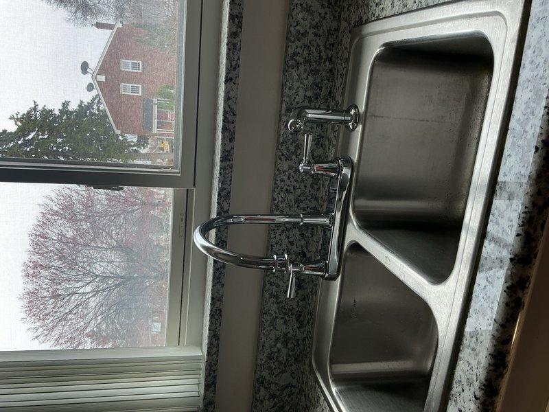 Completed installation of customer-provided kitchen faucet on stainless steel double-basin sink with granite countertop. Removed existing fixture, installed new polished chrome high-arc spout faucet with dual-handle deck-mount configuration, connected supply lines, and tested for proper operation and leak-free performance.