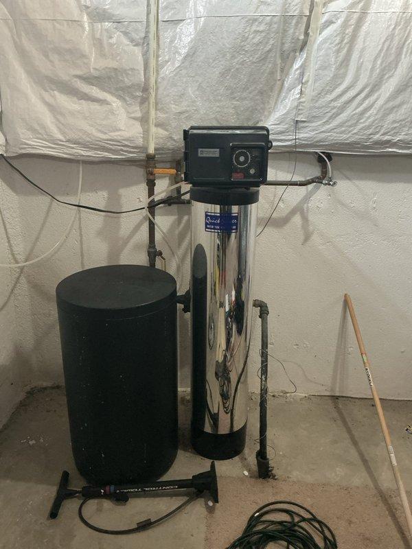 Responded to complaint of low water pressure in multiple areas and sediment in toilet affecting 13-year-old residential property equipped with water softener and reverse osmosis system. Inspected main water supply line at exterior location and evaluated pressure regulator assembly with convergent piping connections. Examined water treatment system consisting of brine tank and stainless steel softener tank with digital control head in utility area. Assessed copper supply lines, valve connections, and pressure regulation components for flow restrictions, sediment accumulation, and proper system operation. Documented existing conditions of filtration equipment and pressure control assembly through photographic evidence for service records.