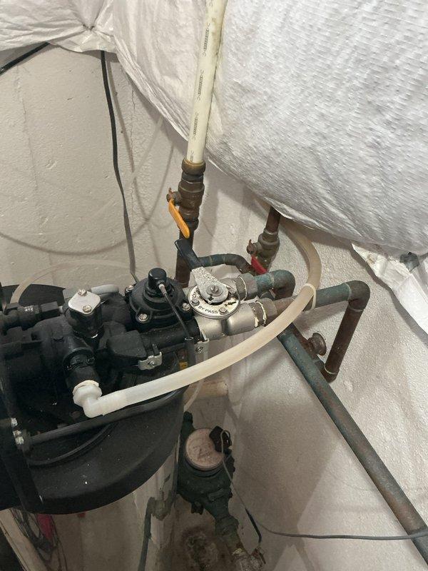 Responded to complaint of low water pressure in multiple areas and sediment in toilet affecting 13-year-old residential property equipped with water softener and reverse osmosis system. Inspected main water supply line at exterior location and evaluated pressure regulator assembly with convergent piping connections. Examined water treatment system consisting of brine tank and stainless steel softener tank with digital control head in utility area. Assessed copper supply lines, valve connections, and pressure regulation components for flow restrictions, sediment accumulation, and proper system operation. Documented existing conditions of filtration equipment and pressure control assembly through photographic evidence for service records.