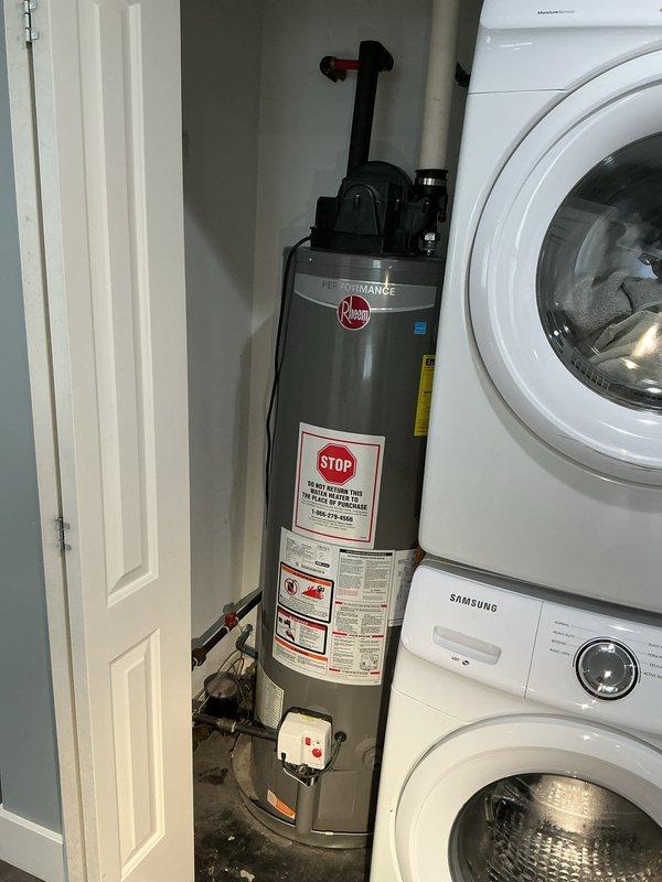 Responded to service call for Rheem Performance gas water heater with pilot light extinguishing on a recurring three-week cycle. Performed diagnostic inspection of the unit located in utility closet adjacent to laundry appliances. Examined thermocouple, gas control valve, pilot assembly, and venting system to identify cause of intermittent pilot failure. Documented equipment condition and configuration with photographic evidence for service records.