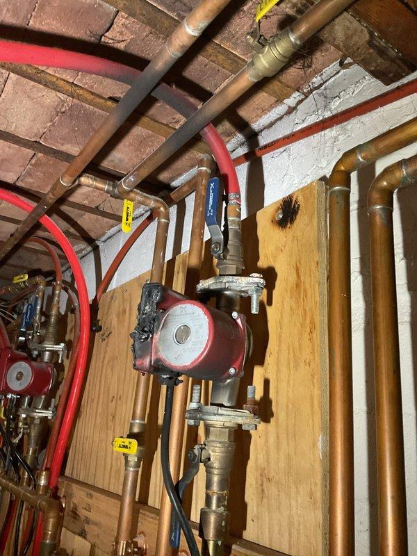 Responded to emergency water pump failure in 1947 residential property affecting hydronic heating system. Upon arrival, assessed damaged circulator pump that had overheated, causing smoke and thermal damage to adjacent water heater components. Replaced failed circulator pump with new unit, installed on plywood mounting panel alongside existing pump in dual-zone configuration. Reconfigured copper and brass piping network to accommodate new pump installation, including integration with existing PEX tubing distribution lines. Installed new shut-off valves with red wheel handles at strategic control points throughout the system for proper isolation capability. Verified all brass fittings and couplings were properly secured and leak-free. Tested both circulation pumps for proper operation and flow direction. Confirmed electrical connections were secure and properly grounded. System pressurized and tested for leaks at all connection points. Verified proper operation of all zone valves and sh