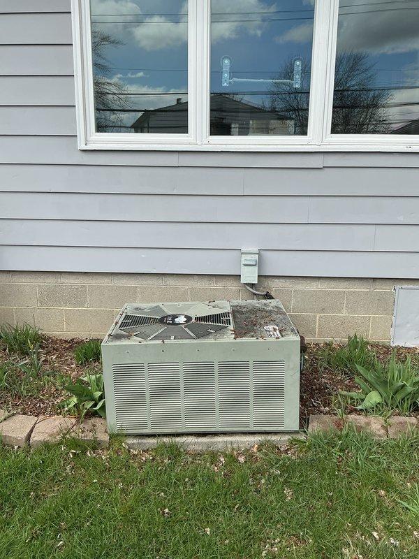 Provided estimate for replacement of non-operational 30-year-old Rheem outdoor air conditioning unit and natural gas furnace system. Unit showed significant deterioration including rust, discoloration, and compromised protective coating on exterior cabinet. Assessed existing installation including refrigerant line penetration through foundation, concrete pad condition, and clearance requirements around equipment positioned in landscaped area near home exterior.