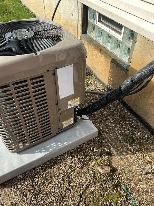 Completed comprehensive Gold AC Inspection on 3-year-old residential air conditioning system with air handler/coil located in basement. Unit confirmed operational at time of inspection. Outdoor condenser unit positioned on concrete pad adjacent to building exterior, properly mounted with adequate clearance for airflow through ventilation slats and top-mounted fan assembly. All visible components including housing, fan guard, electrical conduit, and refrigerant lines appeared intact with normal weathering for equipment age. Advised customer to maintain clear area around condenser unit, removing any debris or animal waste to ensure optimal system performance and prevent potential airflow restrictions or damage to equipment.
