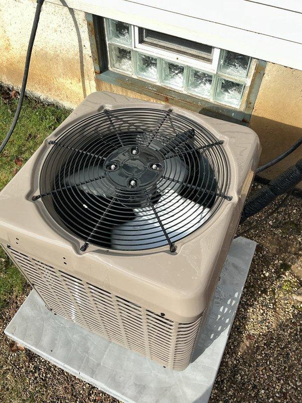 Completed comprehensive Gold AC Inspection on 3-year-old residential air conditioning system with air handler/coil located in basement. Unit confirmed operational at time of inspection. Outdoor condenser unit positioned on concrete pad adjacent to building exterior, properly mounted with adequate clearance for airflow through ventilation slats and top-mounted fan assembly. All visible components including housing, fan guard, electrical conduit, and refrigerant lines appeared intact with normal weathering for equipment age. Advised customer to maintain clear area around condenser unit, removing any debris or animal waste to ensure optimal system performance and prevent potential airflow restrictions or damage to equipment.