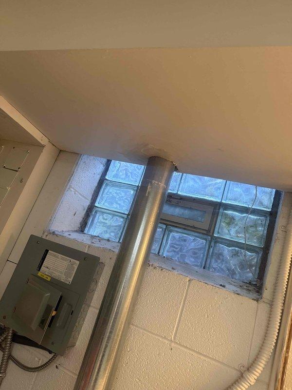 Performed diagnostic inspection of dryer vent system and evaluated drywall damage around vent penetration. Found deteriorated seal and rough opening where cylindrical duct passes through wall/ceiling junction, with exposed drywall edges and gaps compromising air barrier integrity. Documented conditions of metallic ductwork, electrical panel, and glass block windows in mechanical space for repair recommendations.