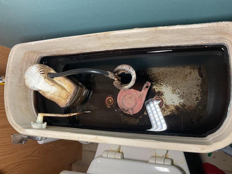 Responded to service call for water heater producing whistling noise and slow-filling toilet tank. Inspected toilet tank and identified significant mineral deposits and hard water buildup throughout interior surfaces, affecting fill valve performance. Fill valve assembly showed signs of age with corroded components and sediment accumulation restricting water flow, causing extended fill times. Flapper valve exhibited mineral buildup and weathering. Examined water heater and diagnosed whistling noise originating from sediment accumulation in tank causing steam pockets during heating cycle. Documented condition of both fixtures with photographs showing extent of mineral deposits and component degradation. Provided recommendations for fill valve replacement, flapper replacement, and water heater tank flushing to restore proper operation and eliminate noise issues.