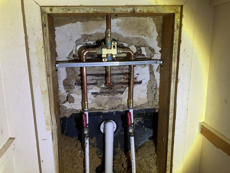 Responded to service call for water heater evaluation and requote. Upon inspection, customer requested alternative solution that would not require cutting into existing wall structure. Documented current plumbing configuration including exposed copper supply lines, PVC piping with shut-off valves, and shower installation within tiled bathroom area. Captured photographic evidence of existing conditions showing wall cavity with visible framing, mounting hardware, and water supply connections for assessment and revised proposal preparation.