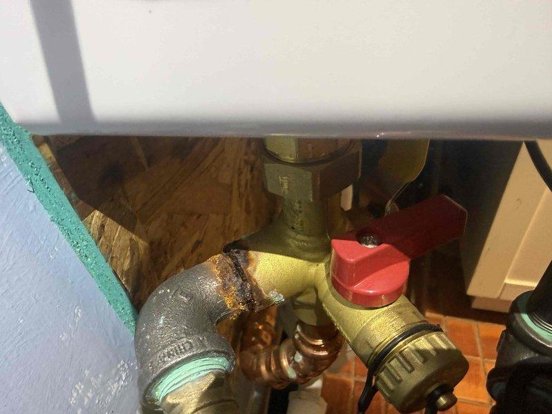 Responded to water leak concern at tankless water heater installation. Upon inspection, discovered significant rust and corrosion around pipe connections, fittings, and brass components at the pressure relief valve assembly. The unit, approximately one year old, showed premature deterioration at threaded connections and elbow joints. Documented corrosion patterns on copper and brass fittings, particularly around the pressure relief valve with red handle and associated piping. Photographed affected areas showing oxidation on metallic surfaces and compromised pipe joints that could lead to future leak points if left unaddressed.