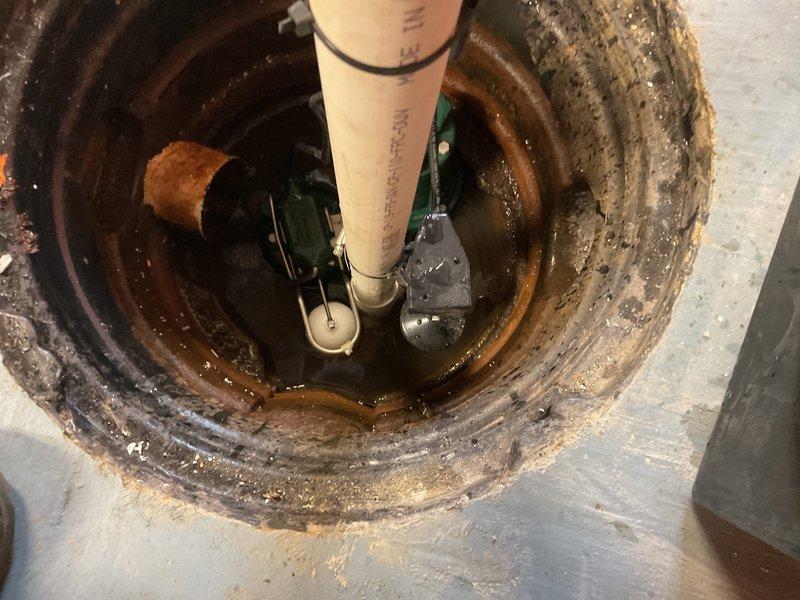 Replaced deteriorated sump pump system in basement pit showing extensive rust, mineral deposits, and corrosion from long-term water exposure. Installed new green submersible pump unit with float switch assembly, connected to existing white PVC discharge piping, and secured all electrical wiring and connections to restore proper water management functionality.