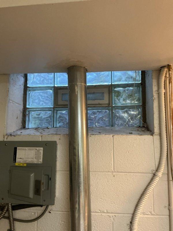 Accessed electrical panel in basement utility area to diagnose and repair electrical system issues. Created ceiling access point to reach conduit and wiring infrastructure above glass block window installation. Addressed electrical concerns related to metal conduit and panel connections in area with white cinder block construction. Documented existing conditions including glass block window damage and electrical panel configuration for repair completion.