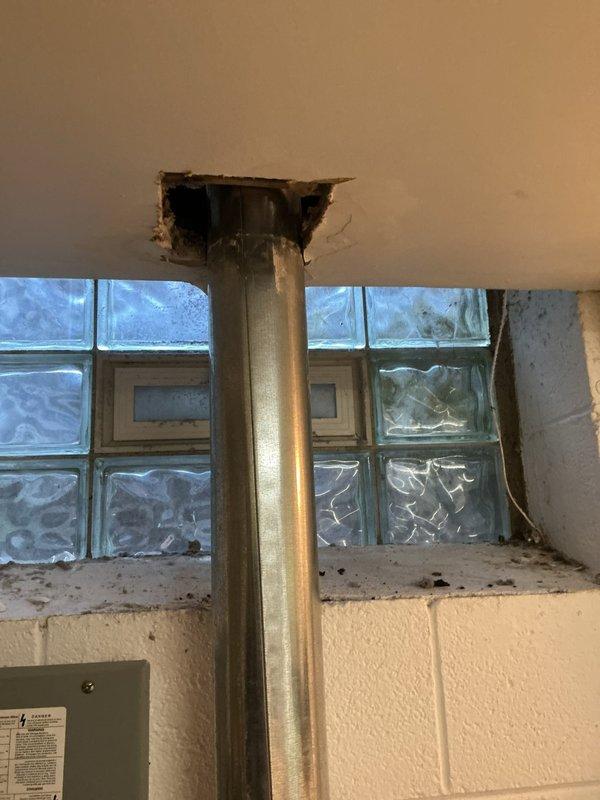 Accessed electrical panel in basement utility area to diagnose and repair electrical system issues. Created ceiling access point to reach conduit and wiring infrastructure above glass block window installation. Addressed electrical concerns related to metal conduit and panel connections in area with white cinder block construction. Documented existing conditions including glass block window damage and electrical panel configuration for repair completion.